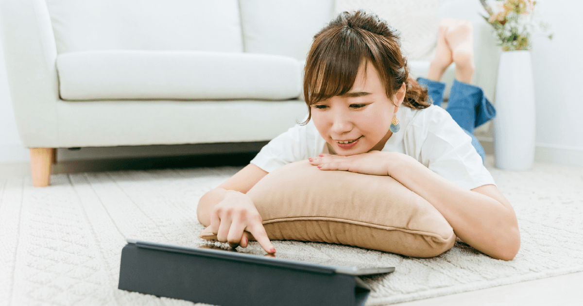 寝転がってタブレットを見る女性