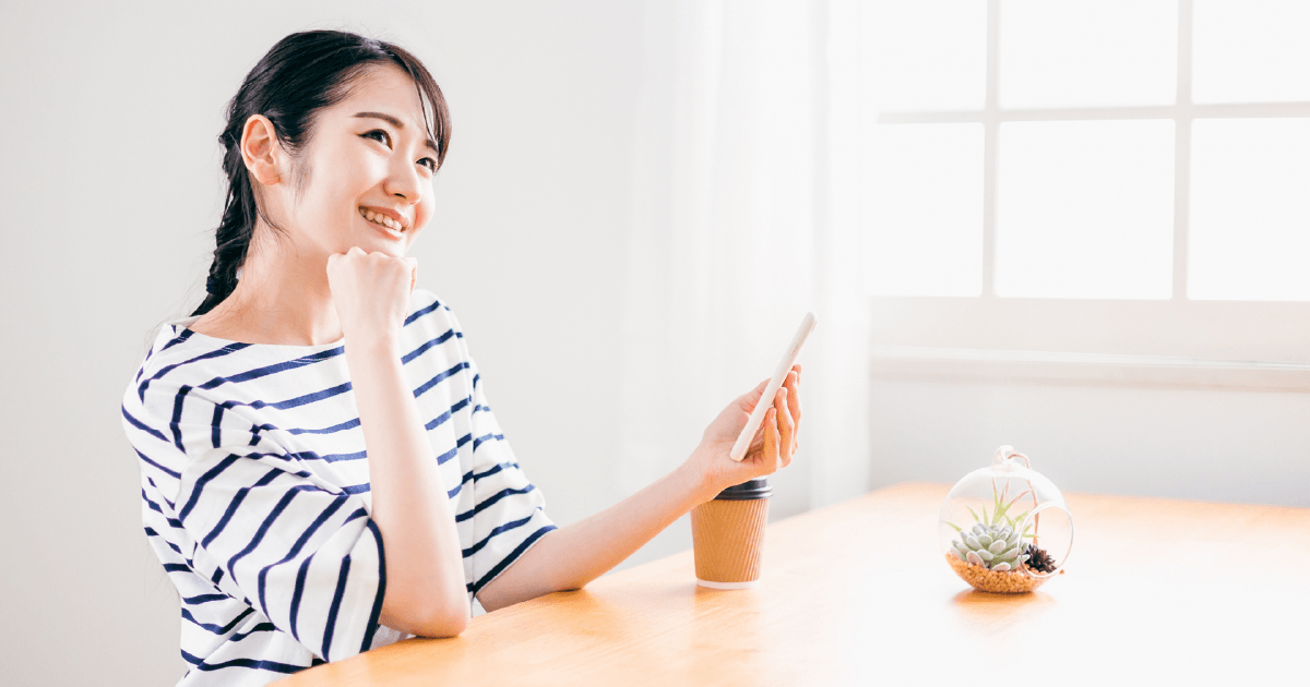 スマホを片手に笑顔で考え事をする女性